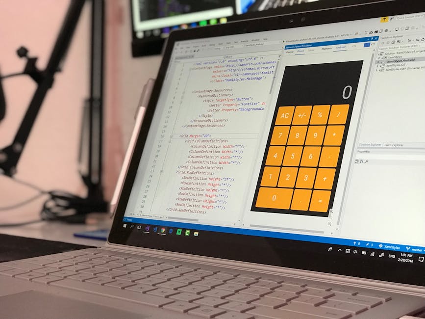 Close-up view of a laptop displaying HTML code on a text editor on the left side of the screen, with a large orange calculator widget on the right. The laptop is situated on a desk, and the background